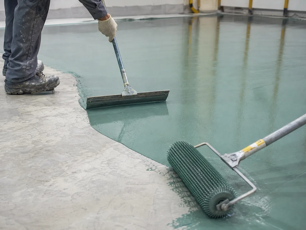 Professional epoxy floor installation in Saudi Arabia using squeegee and spike roller on prepared concrete